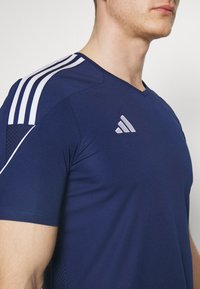 Camiseta deportiva de color azul marino con detalles en rayas blancas en los hombros. Fabricada con un tejido suave que presenta un panel texturizado sutil. Diseño con escote en V.