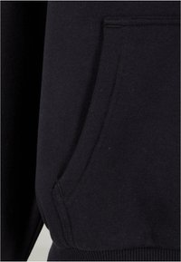 Detalle de sudadera negra que muestra un tejido suave, puños acanalados y un bolsillo tipo canguro con un acabado texturizado. Sin patrones o acentos prominentes.