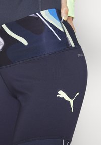 Leggings de sport bleu marine présentant un motif abstrait et coloré. Matière marquée DRYCELL. Logo en vert clair d'un puma bondissant sur la cuisse.