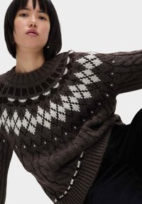 Pullover marrone a maglia con colletto rotondo, caratterizzato da un motivo a diamante bianco e dettagli in lavorazione a treccia lungo l'orlo e le maniche.