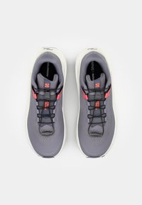 Szare buty sportowe mają siateczkową cholewkę, czarne sznurówki, wyściełany język oraz czerwone akcenty. Podeszwa jest biała z teksturowanym wzorem dla lepszej przyczepności.