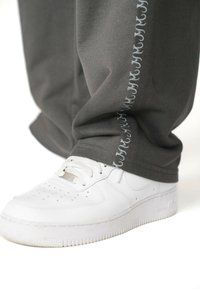 Grijze katoenen sweatpants met een subtiele geborduurde patroon in lichtgrijs aan de zijkant, gecombineerd met witte sport sneakers.