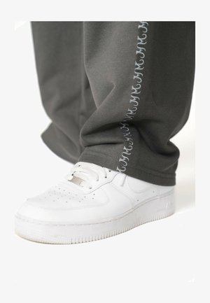 Pantaloni di felpa grigi in cotone con un sottile motivo ricamato grigio chiaro lungo il lato, abbinati a sneaker sportive bianche.