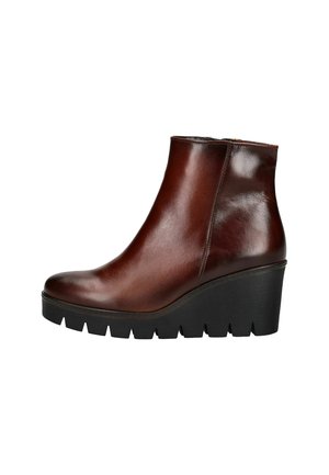 Stivale alla caviglia in pelle marrone con un design elegante, punta rotonda e tacco a cuneo. Presenta una suola in gomma nera con texture. Chiusura con zip laterale.