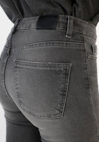 Dark gray denim jeans with a smooth finish, featuring a back pocket and a black leather waistband label with a skull logo.