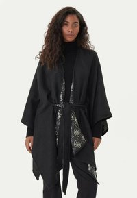 Kimono nero avvolgente con maniche ampie, dotato di una fodera interna a motivi e una cintura in vita. Texture morbida, design versatile.