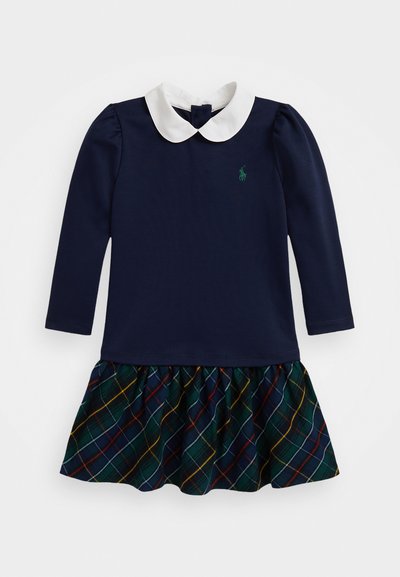 Jūras zila kleita ar baltu apkakli, garām piedurknēm un plandošu svārku zili dzeltenā un sarkanā kārtā. Uz krūšu ir neliels zaļš logos.