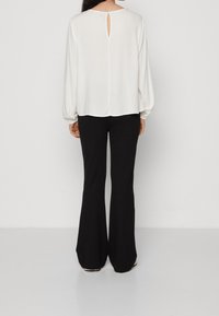 Vit långärmad blus med en nyckelhålsklyfta på ryggen, i kombination med svarta vida byxor. Slätt tyg med mjuk drapering.