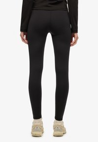 Czarne legginsy o gładkiej, elastycznej fakturze i wysokim stanie, połączone z off-white butami sportowymi. Minimalistyczny design, brak widocznych wzorów.