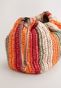 Sac à main tissé multicolore arborant de larges rayures rouges, orange, vertes et crème, avec une anse en cuir lisse marron clair et une fermeture par cordon de serrage.