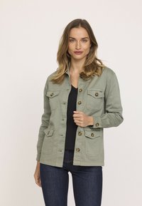 Veste utilitaire vert olive avec quatre poches avant, fermetures à boutons et un col. Fabriquée en tissu léger, elle présente une coupe droite.