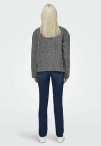 Suéter gris texturizado con un corte relajado, combinado con jeans azul oscuro y zapatillas blancas, visto desde la parte de atrás. Cabello largo y lacio visible.