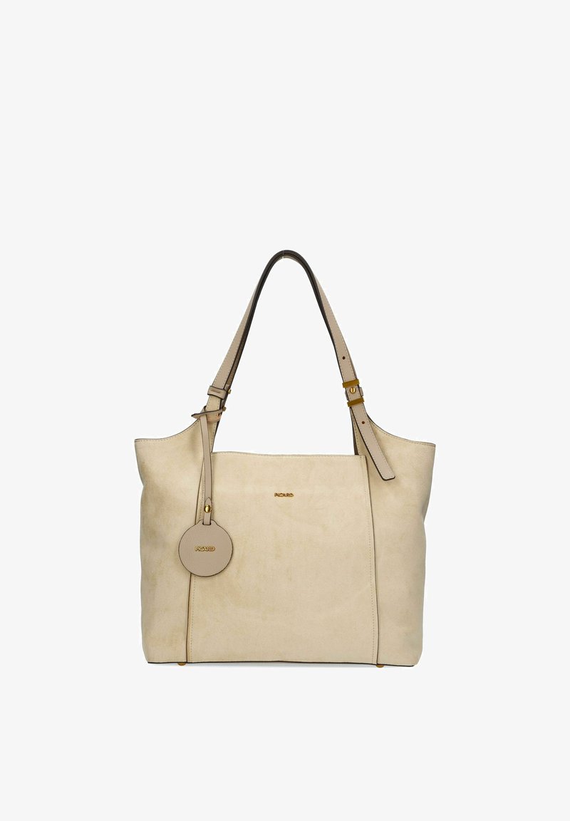 Sac fourre-tout en daim beige avec des sangles d'épaule réglables, une étiquette ronde suspendue et un petit logo de la marque en or au centre avant.
