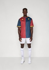 Nogometni dres v bordo in modri barvi z rumenimi poudarki, logotipom Kappa in emblemom leva; kombiniran z belimi kratkimi hlačami in nogavicami.