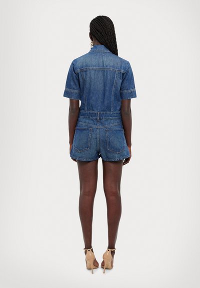 Denim overal s krátkym rukávom a priliehavým pásom, zobrazený zo zadnej strany. Tmavomodrý odtieň s dvoma zadnými vreckami a zakončenými šortkami.