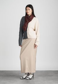 Sweater com design de malha em cabos cinza e creme; saia midi bege; cachecol bordô; saltos pretos com tiras e meias brancas. Fundo simples.