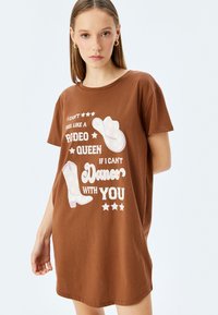 Vestido de algodón marrón con camiseta que presenta un texto gráfico blanco e ilustraciones de un sombrero de vaquero y botas, con acentos de estrellas. Manga corta y corte relajado.