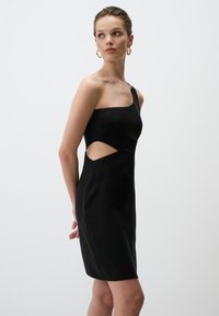 Schwarzes, einseitiges Kleid mit taillierter Silhouette und Ausschnitt in der Taille. Glattes Gewebe mit subtiler schimmernder Optik.