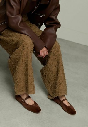 Bruine suède Mary Jane schoenen met een vierkante neus, voorzien van een enkele gesp, gecombineerd met getextureerde, ruige bruine broek.