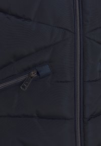 Navy modrá péřová bunda s diagonálním šitím, s předním zipem a bočními kapsami na zip, vyrobená z hladkého, lehkého materiálu.