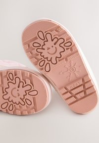 Suole di scarpe in gomma rosa chiaro con un design giocoso a schizzi e una faccina sorridente, texturizzate con vari motivi per aderenza e trazione.