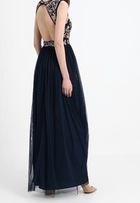 Mörkblå aftenkjol med blommönstrad bodice, öppen rygg och flödande tyllkjol, kompletterad med en åtsittande midja.