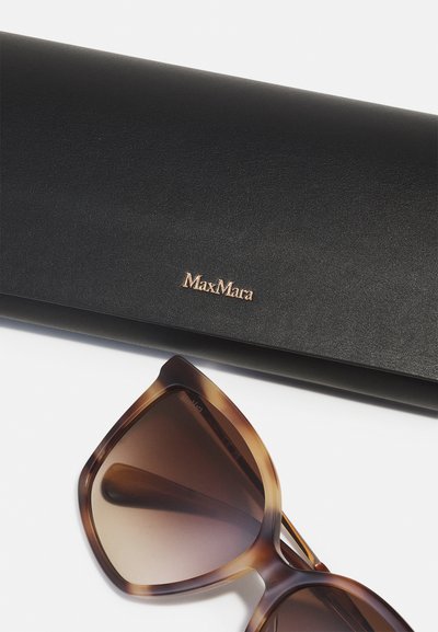 MaxMara-aurinkolasit ruskeasävyisillä linsseillä ja kilpikonnakuosisella kehykset, esillä mustan nahkakannellisen kanssa, jossa on kultainen logo.