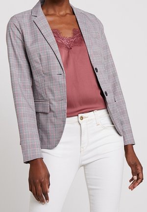 Grijze geruite blazer met rode accenten, sluiting met één knoop, en twee zijzakken, gedragen over een mauve camisole en witte jeans.
