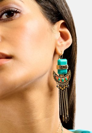 Boucle d'oreille statement bleu sarcelle et or avec un design géométrique, des accents métalliques complexes et des chaînes pendantes, mettant en valeur un mélange de textures.