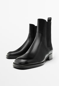 Bottes noires en cuir avec panneaux latéraux élastiques, bouts arrondis et talons carrés texturés. Fini lisse au design minimaliste.