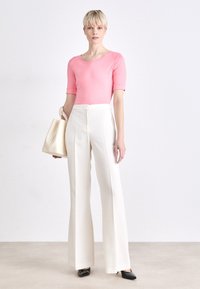 Lichtroze getailleerde top gecombineerd met hoge, witte broeken. Zwarte puntige schoenen en een crèmekleurige handtas. Eenvoudige, gestructureerde en op maat gemaakte look.