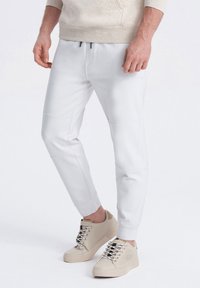 Witte tapered joggers met gestikte accenten en een elastische tailleband, gecombineerd met beige sneakers met geperforeerde details en veters.
