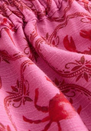 Tissu rose avec un tissage texturé, présentant un motif de crabes rouges et d'éléments floraux. Le tissu est froncé en haut.