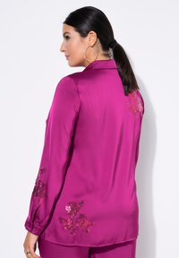 Fuchsia silke skjorte med lange ærmer, broderede blomsterdetaljer i nuancer af pink og bordeaux på ryggen og ærmerne. Glat tekstur.