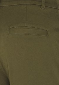 Olivgröna byxor med ett bakfack som har en rak sömsöm och en slät, texturerad tyg.
