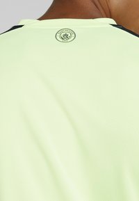 Lysegrøn atletisk trøje med en tekstureret overflade, med rund hals og en sort detalje langs skuldrene. Manchester City-logo på ryggen.