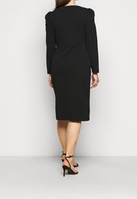 Svart midiklänning med långa ärmar, puffiga axeldetaljer och en figurnära design. Bärs med svarta sandaletter med klack.