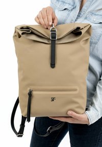Beige Rolltop-Rucksack aus strapazierfähigem Material, mit einem schwarzen Tragegurt und Beschlägen, einer vorderen Reißverschlusstasche und Logodetails.