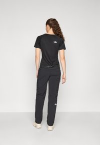 T-shirt et pantalon de sport noirs, avec un logo au dos, conçus avec une coupe ajustée et un tissu léger pour un confort optimal.