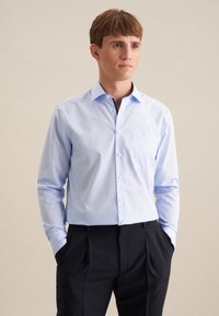 Camicia a maniche lunghe azzurro chiaro con tasca, design con colletto e texture liscia, abbinata a pantaloni scuri.