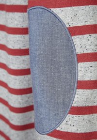 Koszulka bawełniana w szare i czerwone poziome paski, z niebieską dżinsową łatą na rękawie. Miękka tekstura i swobodny design.