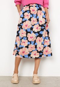 Floraler Midi-Rock mit großen rosa und blauen Blumen auf schwarzem Hintergrund, einem elastischen Bund und einem fließenden Schnitt. Kombiniert mit beigen Schuhen.