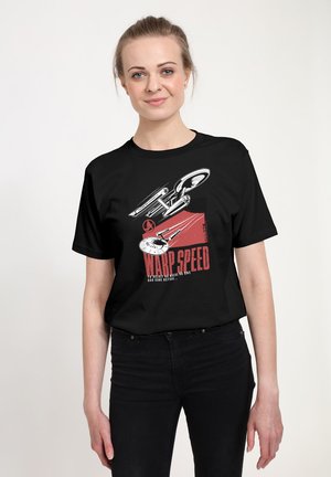 Kvinde iført en sort T-shirt med et hvidt og rødt Star Trek rumskibsdesign og teksten "Warp Speed" på forsiden.