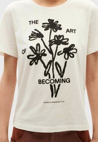White cotton t-shirt featuring a black graphic of flowers with the text "THE ART OF BECOMING." Short sleeves and a crew neckline.
