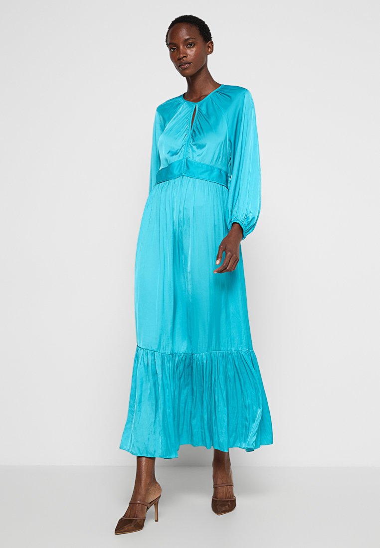 Langärmliges, knielanges Kleid aus leuchtender türkisfarbener Satin. Es hat ein gerafftes Oberteil, einen plissierten Ausschnitt und einen ausgestellt Rock mit Rüschen.