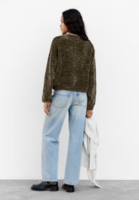 Maglione verde a maglia con finitura texture, vestibilità ampia e orlo a costine, abbinato a jeans a gamba larga blu chiaro e stivaletti neri.
