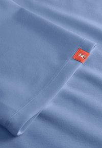Lichtblauwe katoenen t-shirt met een gladde textuur, met een klein rood etiket met een hondenlogo aan de zijkant.