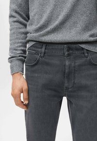 Vaqueros gris oscuro con una textura lisa de mezclilla, que presentan un diseño clásico de cinco bolsillos y un cierre con botón en la cintura.