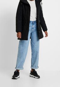 Svart vadderad parka med huva, grå t-shirt, ljusblå högmidjade jeans och svarta sneakers med vita detaljer, avslappnad passform, uppvikta fållar.