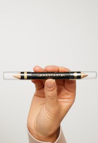 Crayon noir à double extrémité avec des capuchons transparents, des accents dorés et le texte "ANASTASIA BEVERLY HILLS". Une extrémité a une pointe aiguisée, l'autre est rétractable.